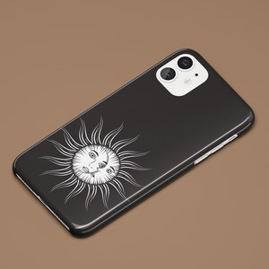 May include: Black phone case with a white sun design featuring a face with two eyes. The phone case has a white camera bump with two black camera lenses.