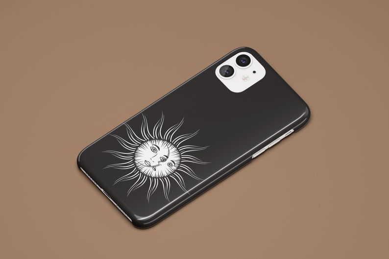 May include: Black phone case with a white sun design featuring a face with two eyes. The phone case has a white camera bump with two black camera lenses.