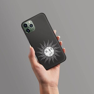 May include: Black phone case with a white sun and face design. The sun has a face with three eyes.
