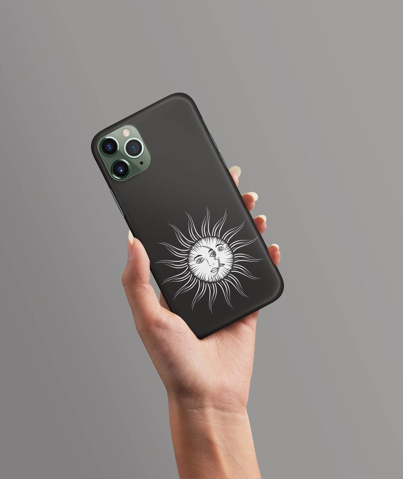May include: Black phone case with a white sun and face design. The sun has a face with three eyes.