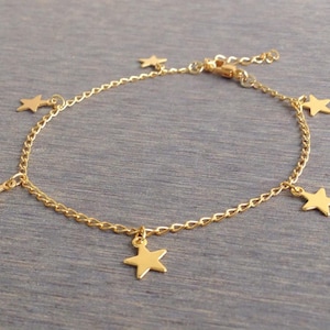 Puede incluir: Un tobillo de cadena dorada con cinco colgantes de estrellas.