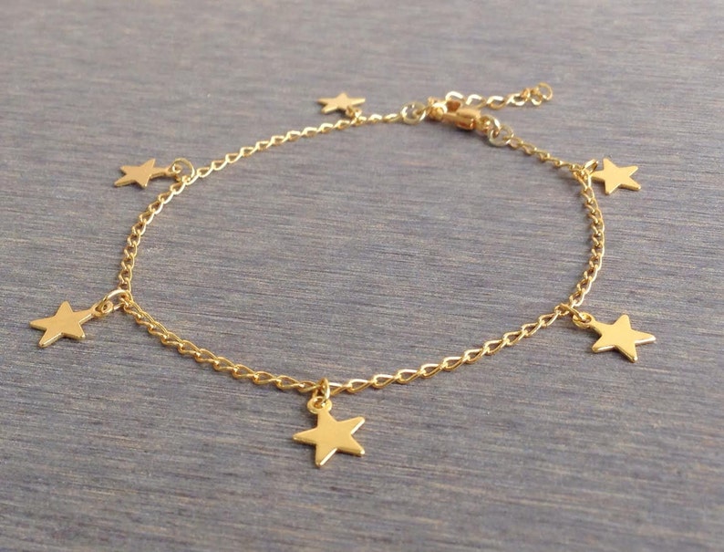 Puede incluir: Un tobillo de cadena dorada con cinco colgantes de estrellas.