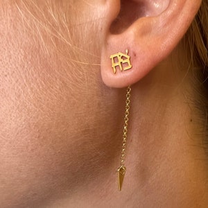 May include: Gold dangle earrings with a small square charm featuring the Chinese character "房" and a long chain ending in a small triangle charm.