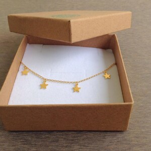 Puede incluir: Un collar de cadena dorada con cinco colgantes de estrellas en una caja de cart&oacute;n marr&oacute;n con interior blanco.