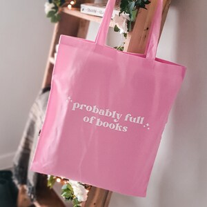 May include: Pink tote bag with white text that reads "probably full of books" and small white stars on either side of the text.
