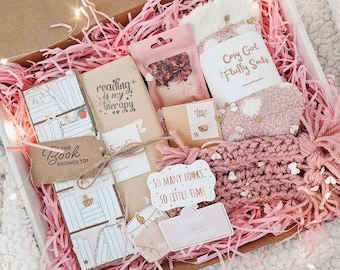 Puede incluir: Una caja de regalo llena de papel triturado rosa, libros, un par de calcetines rosas esponjosos y otros pequeños regalos. La caja incluye una etiqueta que dice "This Book Belongs To" y otra que dice "So Many Books, So Little Time."