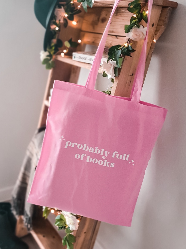May include: Pink tote bag with white text that reads "probably full of books" and small white stars on either side of the text.