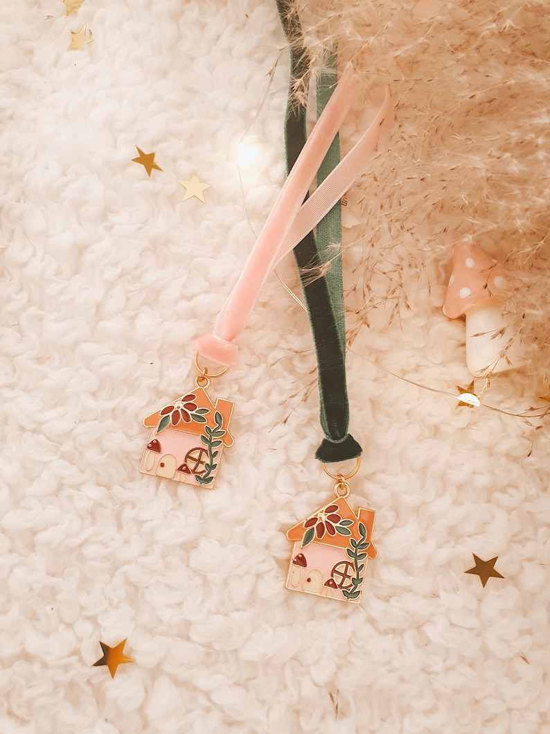 May include: Two pink and orange enamel house charms with green vines and mushroom details, attached to pink and green velvet ribbons.