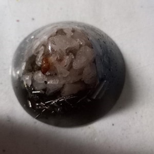 May include: A black and silver pyramid-shaped pendant with a clear resin top containing pink and white crystals.