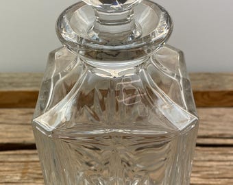 May include: A clear glass decanter with a faceted stopper. The decanter has a square body with a cut glass design.