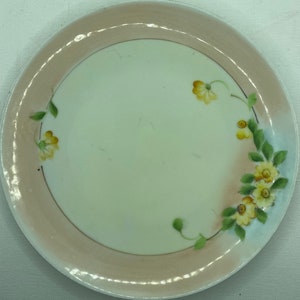 May include: A white porcelain plate with a pink rim and a floral design featuring yellow flowers and green leaves.