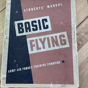 May include: A vintage "Basic Flying" Students' Manual with a cover design in navy blue and dusty rose. The title "BASIC FLYING" is in bold white text. The text "ARMY AIR FORCES TRAINING COMMAND" is also visible, along with a star graphic.