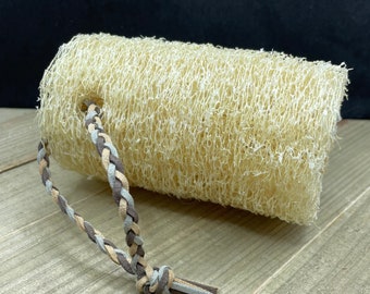 May include: A natural loofah sponge with a braided leather strap. The loofah is light brown and the strap is brown and beige.