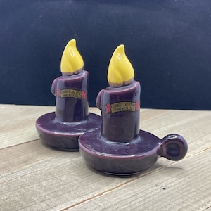 Puede incluir: Dos candelabros de cerámica púrpura con llamas amarillas y etiquetas rojas y doradas que dicen "Alexander Lake Lodge Grand Mesa Colo".