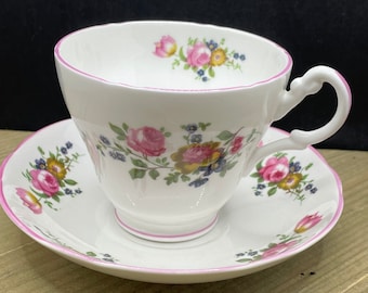 May include: A white teacup and saucer with a pink floral pattern. The cup and saucer have a pink trim.