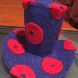 May include: A quirky, handmade top hat crafted from deep blue felt, decorated with large, bright red polka dots. The hat has a wide brim and a cylindrical crown, suitable for fancy dress or play.