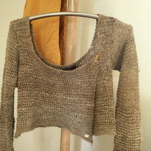 May include: A brown crocheted sweater with long sleeves and a scoop neck. The sweater is hanging on a wooden hanger.