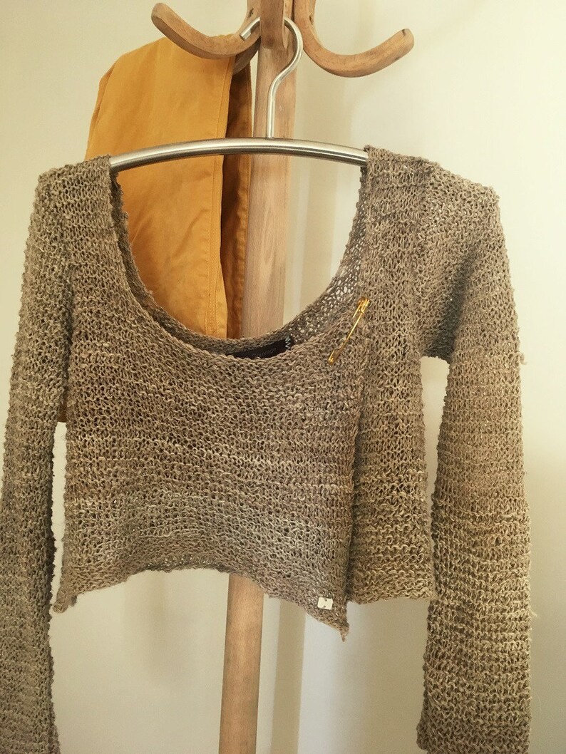 May include: A brown crocheted sweater with long sleeves and a scoop neck. The sweater is hanging on a wooden hanger.
