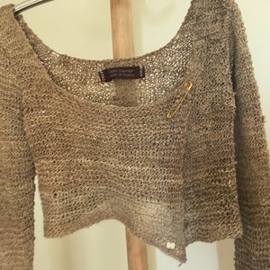 May include: A brown crocheted cardigan with a safety pin closure. The cardigan is made of a loose knit fabric and has a relaxed fit.