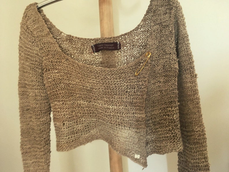 May include: A brown crocheted cardigan with a safety pin closure. The cardigan is made of a loose knit fabric and has a relaxed fit.
