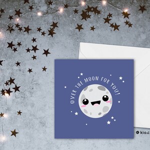 May include: A square greeting card with a cartoon moon illustration on a blue background. The text "OVER THE MOON FOR YOU!" surrounds the moon. A white envelope is next to the card. The background has star-shaped confetti.