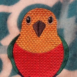 May include: Embroidered patch of a parrot with a red body, yellow head, and green wings and feet. The parrot has black eyes and a black beak.