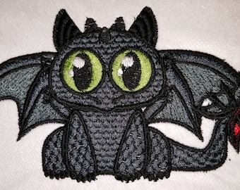 May include: Embroidered patch of a cartoon black dragon with large green eyes and red wings. The dragon is sitting with its wings spread out.