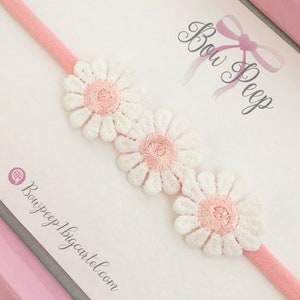 May include: A pink headband with three white daisy-shaped flowers with pink centers. The headband is on a white background with the text "Bow Peep" written in pink cursive.
