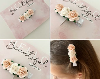 Puede incluir: Una pinza para el pelo con tres flores de tela rosa y blanca. La pinza está sobre un fondo rosa con el texto "Hello Beautiful xoxo".