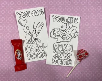 May include: Two blank coloring cards with the text "You are craw-some" and "You are Mardi Gras-some". The card with the crawfish has a heart balloon above it. The card with the Mardi Gras mask has a jester's hat and beads. A red candy bar and a lollipop are in the background.