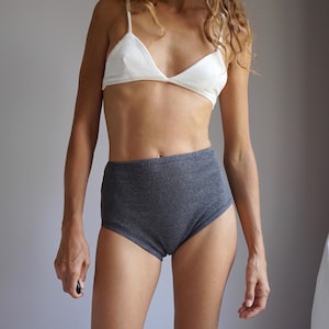 May include: A two-piece set consisting of a white triangle bralette with thin shoulder straps and high-waisted dark gray ribbed briefs. The bralette features a simple triangular cup design, while the briefs have a textured, ribbed fabric finish.
