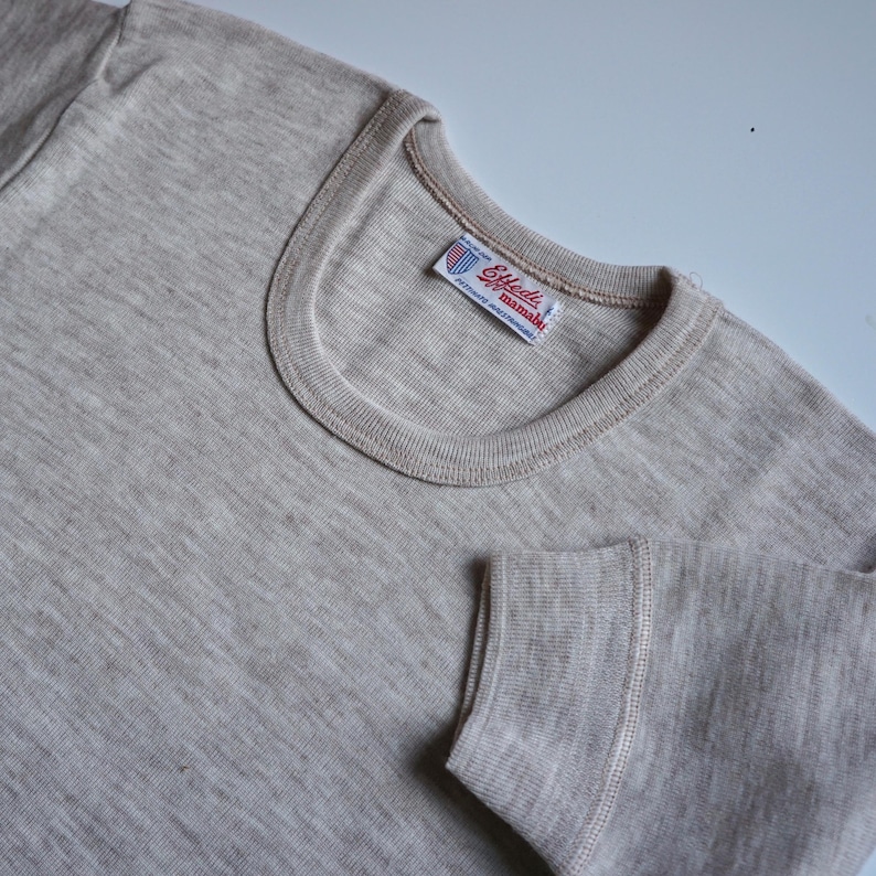 May include: A light grey long-sleeved shirt with a white tag that reads "Enell's" and "manmade fibres" in red lettering.