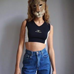 May include: A black and white cropped tank top with yellow accents. The tank top has the text "BASIC ATHLETIC" printed on the front. The model is wearing blue jeans.