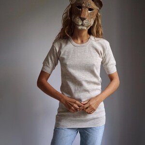 May include: A person wearing a light grey, short-sleeved t-shirt with a lion mask.