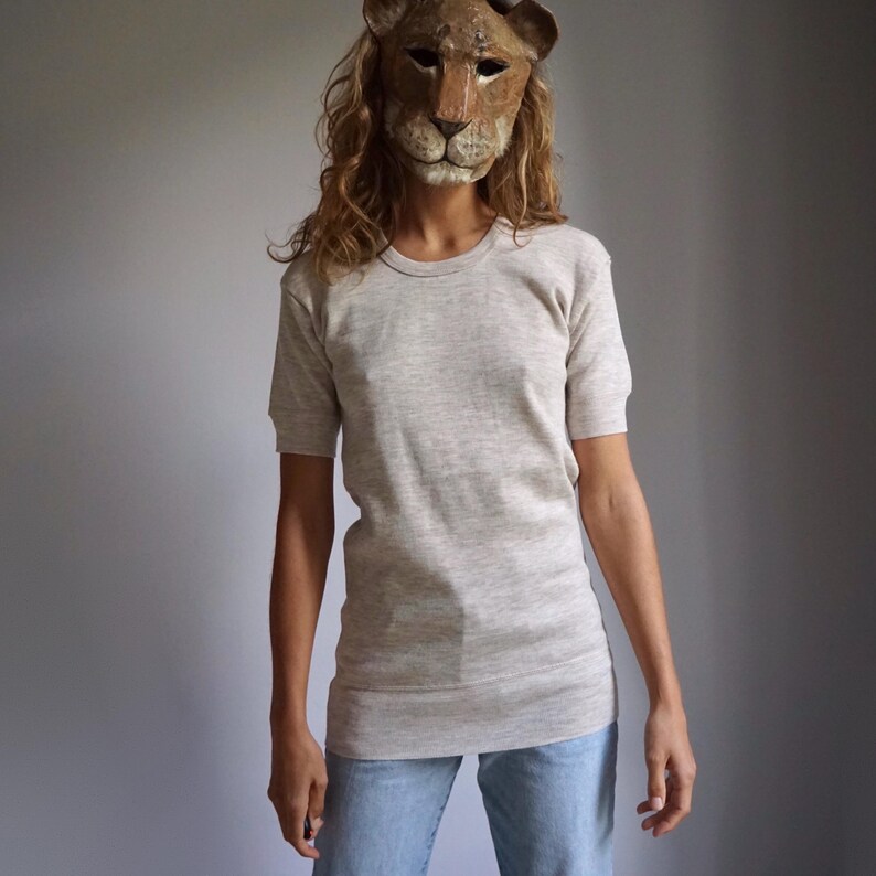 May include: A person wearing a light grey, long-sleeved t-shirt with a crew neck. The person is wearing blue jeans and a lion mask.