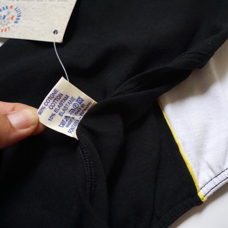 May include: A black and white striped shirt with a yellow stripe. The shirt has a tag that reads "90% Cotone Cotton 10% Elastam Elastane Made in Italy by Fontana Pignatti".