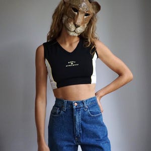 May include: A black and white cropped tank top with the text "BASIC & ATHLETIC" in yellow. The tank top has a white stripe on the side and is worn with blue jeans.