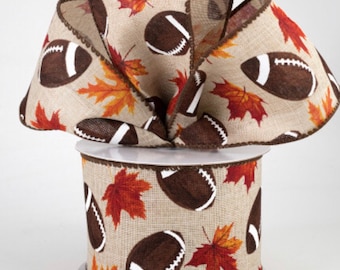 May include: A spool of tan burlap ribbon featuring a repeating pattern of brown footballs with white laces and orange and red autumn maple leaves. The ribbon has dark brown stitched edges and is arranged in a large, multi-looped bow.