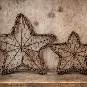 May include: Two rustic, star-shaped decorative objects. The stars are constructed from a woven, brown material, with a wire mesh interior. The larger star is approximately 18 inches across, while the smaller one is about 12 inches. They rest on a wooden shelf.