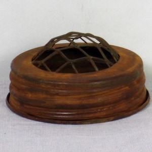 May include: A vintage, rusty brown flower frog with a domed wire grid. The frog has a circular base with ribbed sides and a wire grid top for arranging flowers. The metal has a weathered appearance, suggesting age and use. This item is ideal for floral arrangements.