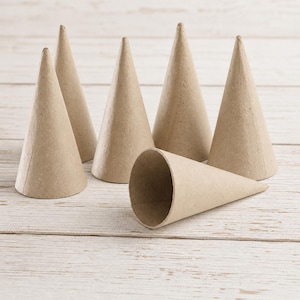 May include: Six brown paper cones of varying sizes are arranged on a light-colored wooden surface. Five cones stand upright, while one lies on its side, revealing its hollow interior. The cones are made of a light brown, textured paper.