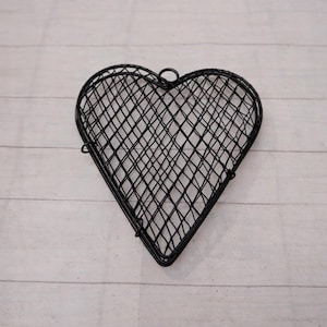 May include: A black metal heart-shaped basket with a diamond-patterned mesh design. The basket has a small loop at the top for hanging. The heart-shaped basket is a decorative item.