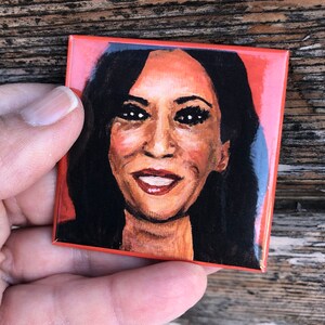 May include: A close-up portrait of a woman with dark hair and brown eyes. She is wearing a red background and has a warm smile.