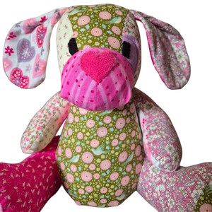 Könnte beinhalten: Ein Patchwork-Plüschtierhund aus rosa, grünem und weißem Blumenstoff. Der Hund hat eine rosafarbene herzförmige Nase und schwarze Augen.