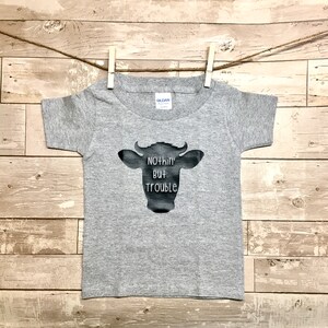 Peut inclure: T-shirt &agrave; manches courtes gris avec une silhouette noire de vache et le texte "Nothin' But Trouble".