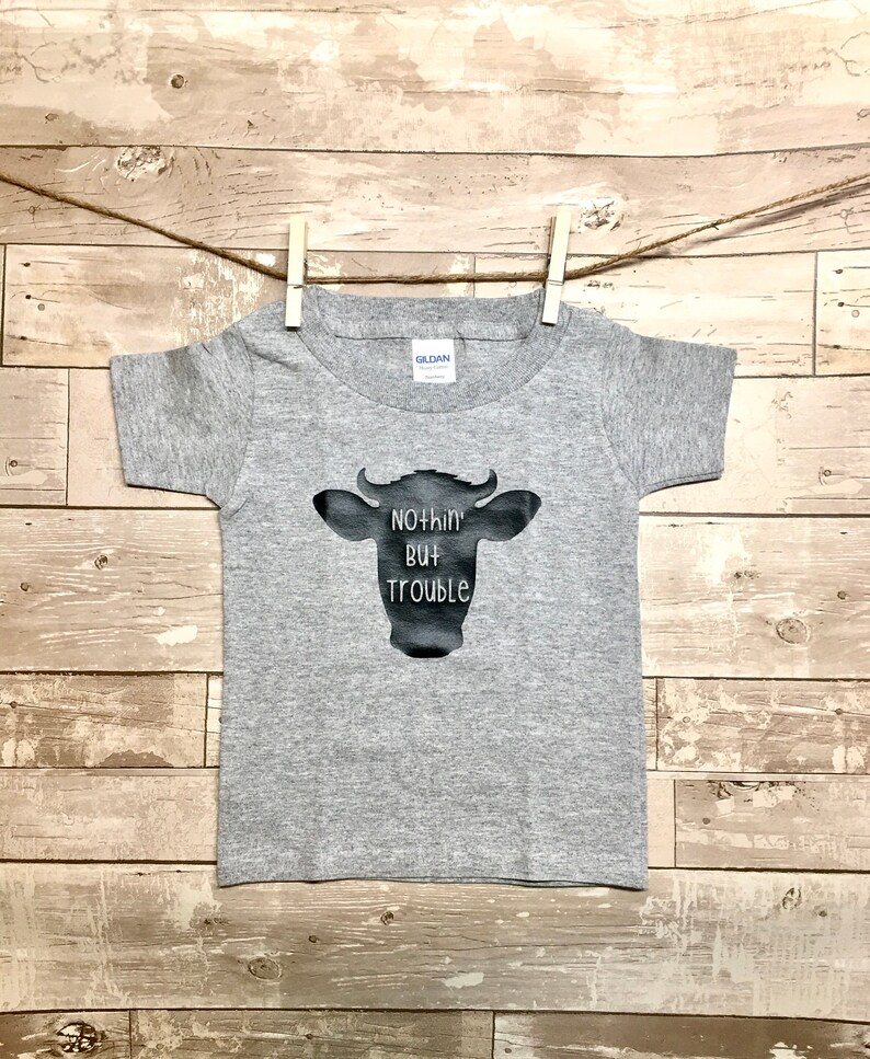 Peut inclure: T-shirt &agrave; manches courtes gris avec une silhouette noire de vache et le texte "Nothin' But Trouble".