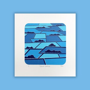 May include: A square art print with a patchwork landscape design in various shades of blue. The artwork shows geometric shapes with dark blue cloud-like forms. The print is on white paper with the title "Patchwork Landscape" and artist's signature.