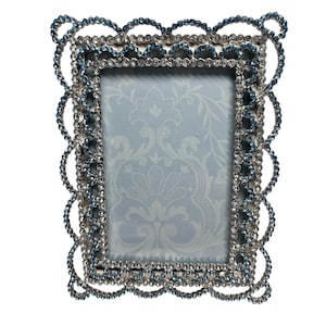 May include: A rectangular picture frame featuring a scalloped edge design adorned with rows of small, sparkling clear crystals and light blue crystals. The center of the frame contains a light blue insert with a subtle, repeating floral damask pattern.