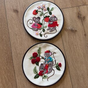 May include: Two circular embroidery hoops featuring off-white fabric. The top hoop displays two grey mice with pink and red clothing picking strawberries. The bottom hoop shows two grey mice in blue and red outfits harvesting red raspberries.