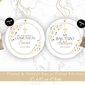 May include: Two round white tags with gold trim and white flowers. The text on the tags reads "Mi Primera Comunión Emma 05.13.2024" and "Mi Bautizo Addison 04.13.2024".